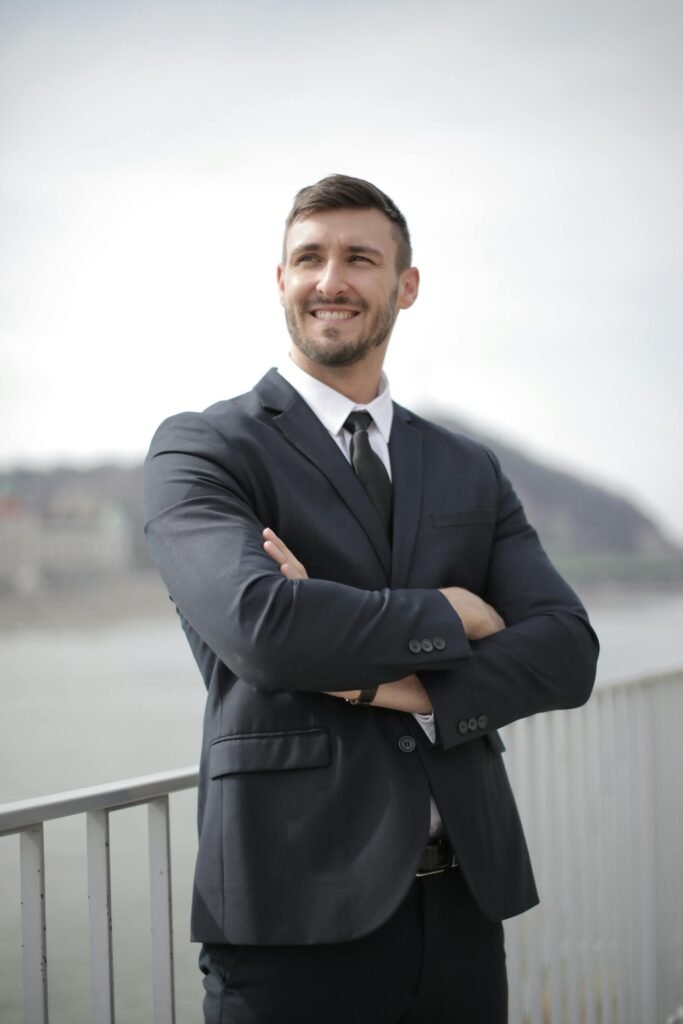 Smiling businessman in a suit standing confidently outdoors by the river.